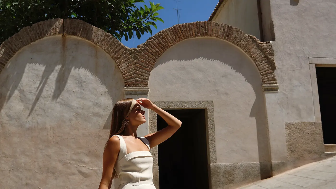 Una viaggiatrice si ripara gli occhi sotto un muro dove antichi archi di mattoni sono stati intonacati e inglobati in un edificio ancora in uso