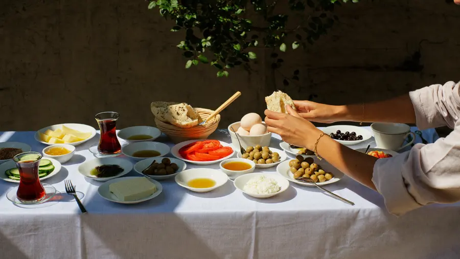 Mani che si allungano su un tavolo assolato pieno di piattini di formaggio, olive, pomodori e pane