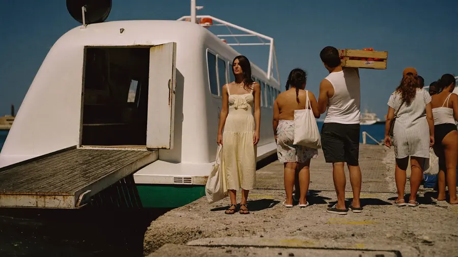 Cestovatelka čeká na nalodění na malý ostrovní trajekt za řadou místních lidí s nákupními taškami a bednou rajčat