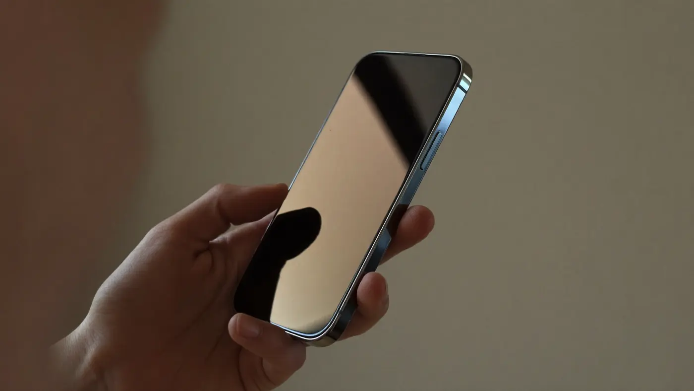 Vista ravvicinata di due mani che tengono uno smartphone moderno inclinato, lo schermo scuro e a specchio