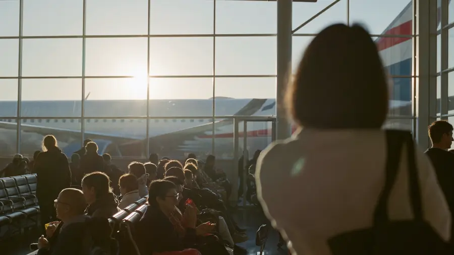 Un gate d'imbarco affollato in un sole caldo e basso, file di passeggeri in attesa e un aereo oltre la vetrata