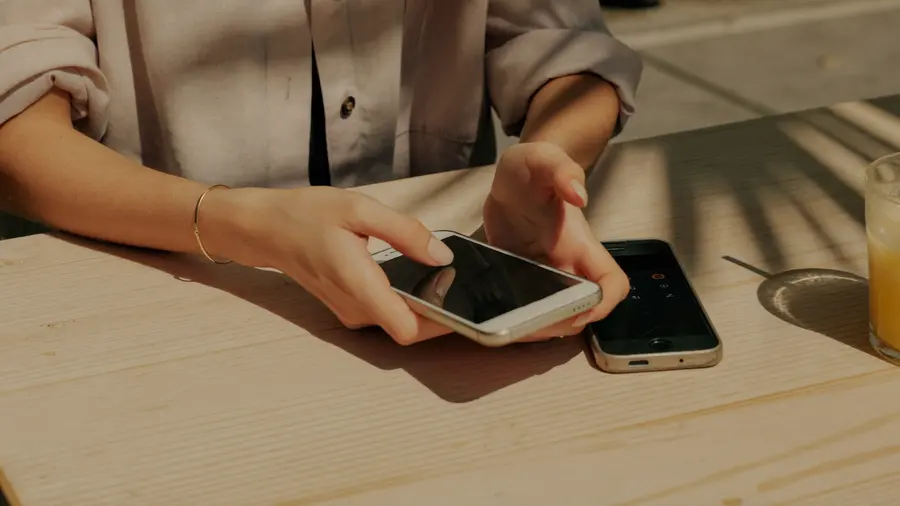 Ženské ruce spouštějí nový telefon ke staršímu, který leží na sluncem prohřátém stolku v kavárně